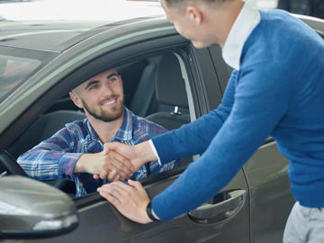 Eine Person in einem blauen Pullover schüttelt die Hand eines Fahrers, der im Auto sitzt, was auf einen Deal oder eine Vereinbarung bei Autoankauf Northeim hinweist.